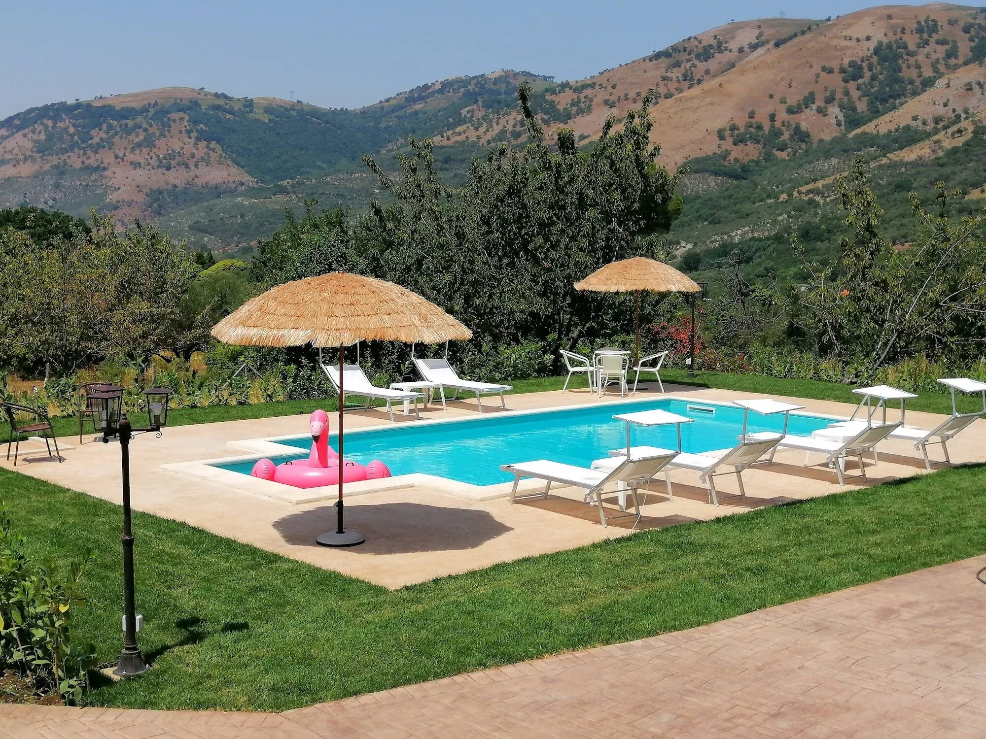 La piscina della Dimora tra il prato, gli ombrelloni di paglia e le colline della Valle Caudina